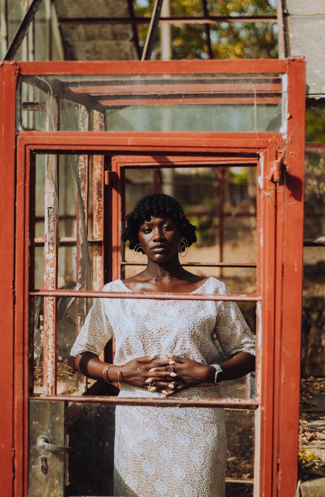 A thoughtful portrait of a woman standing in a rustic glass frame in an outdoor setting.