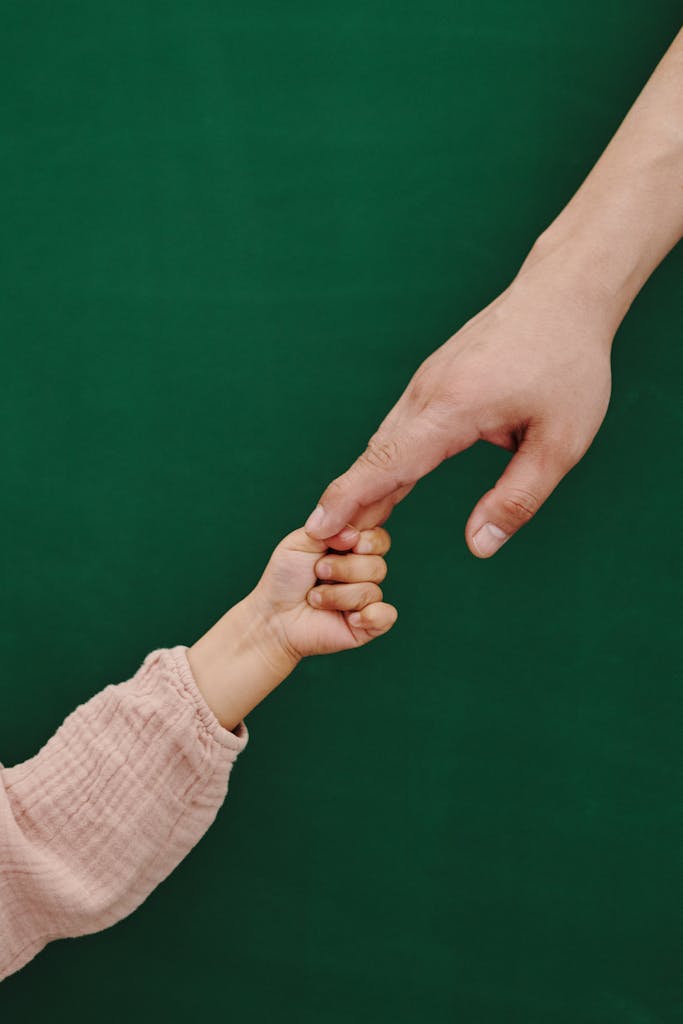 A touching moment of adult and child holding hands with green backdrop.